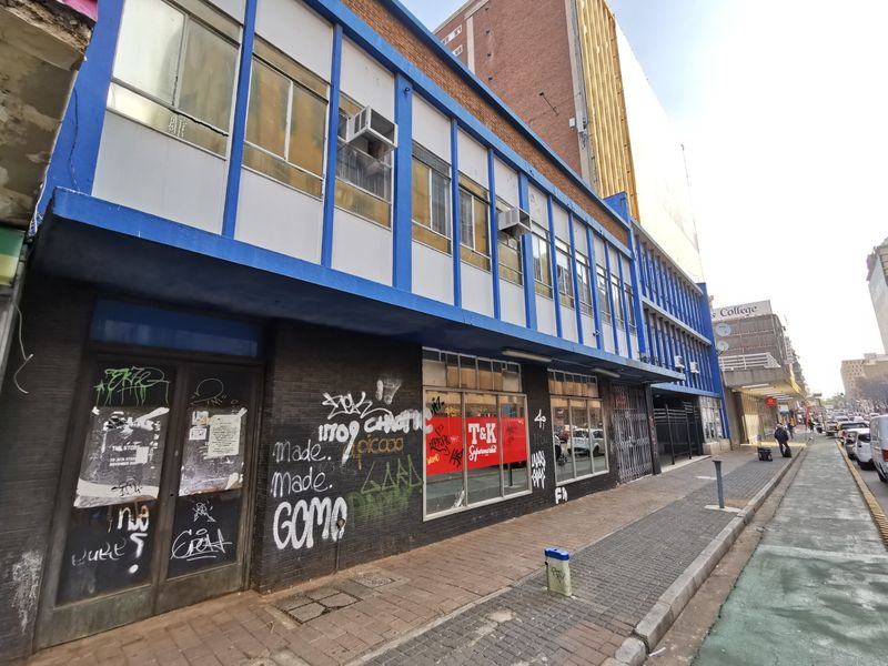 Commercial street-level storefront featuring large display windows and metal security gates, currently showing significant signs of exterior wear and graffiti.