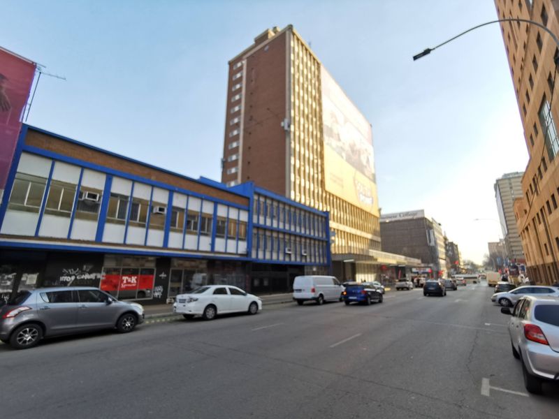 Street-level view of a multi-story commercial building featuring retail frontage and a large advertising billboard in an urban setting.