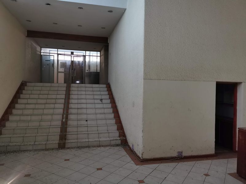 Commercial building entrance foyer featuring a tiled staircase, recessed lighting, and glass entry doors, currently showing signs of wear and debris.