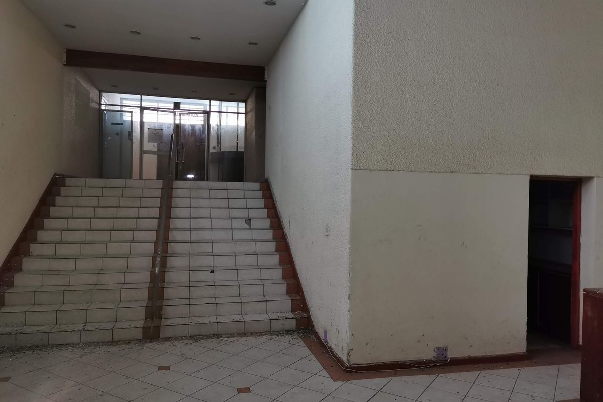 Commercial building entrance foyer featuring a tiled staircase, recessed lighting, and glass entry doors, currently showing signs of wear and debris.