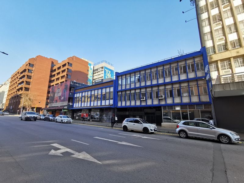 Street-level view of a multi-story commercial building featuring a blue-framed facade, large storefront windows, and integrated window air conditioning units.