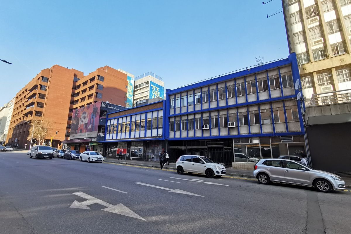Street-level view of a multi-story commercial building featuring a blue-framed facade, large storefront windows, and integrated window air conditioning units.