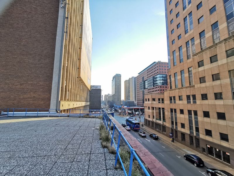 Elevated urban view from a paved terrace overlooking a busy city street and surrounding commercial high-rise buildings.