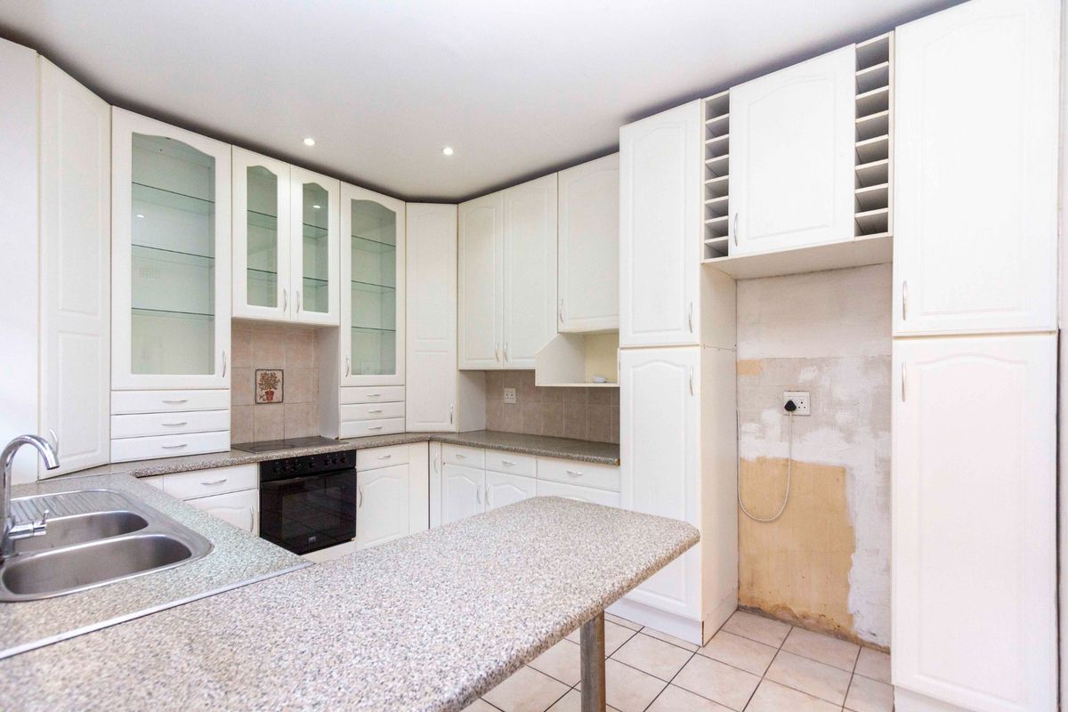 Kitchen featuring white cabinetry, granite-look countertops, integrated oven, and hob. The space requires wall repairs and minor maintenance to restore its finish.