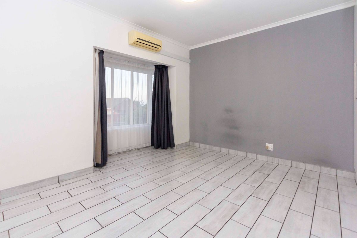 A bright, empty bedroom featuring tiled flooring, a grey accent wall, and a wall-mounted air conditioning unit.