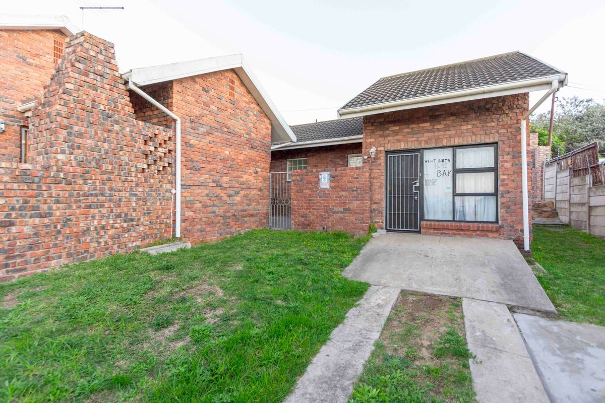 Rear exterior view of a brick house featuring a small lawn, concrete driveway, and security gate access.
