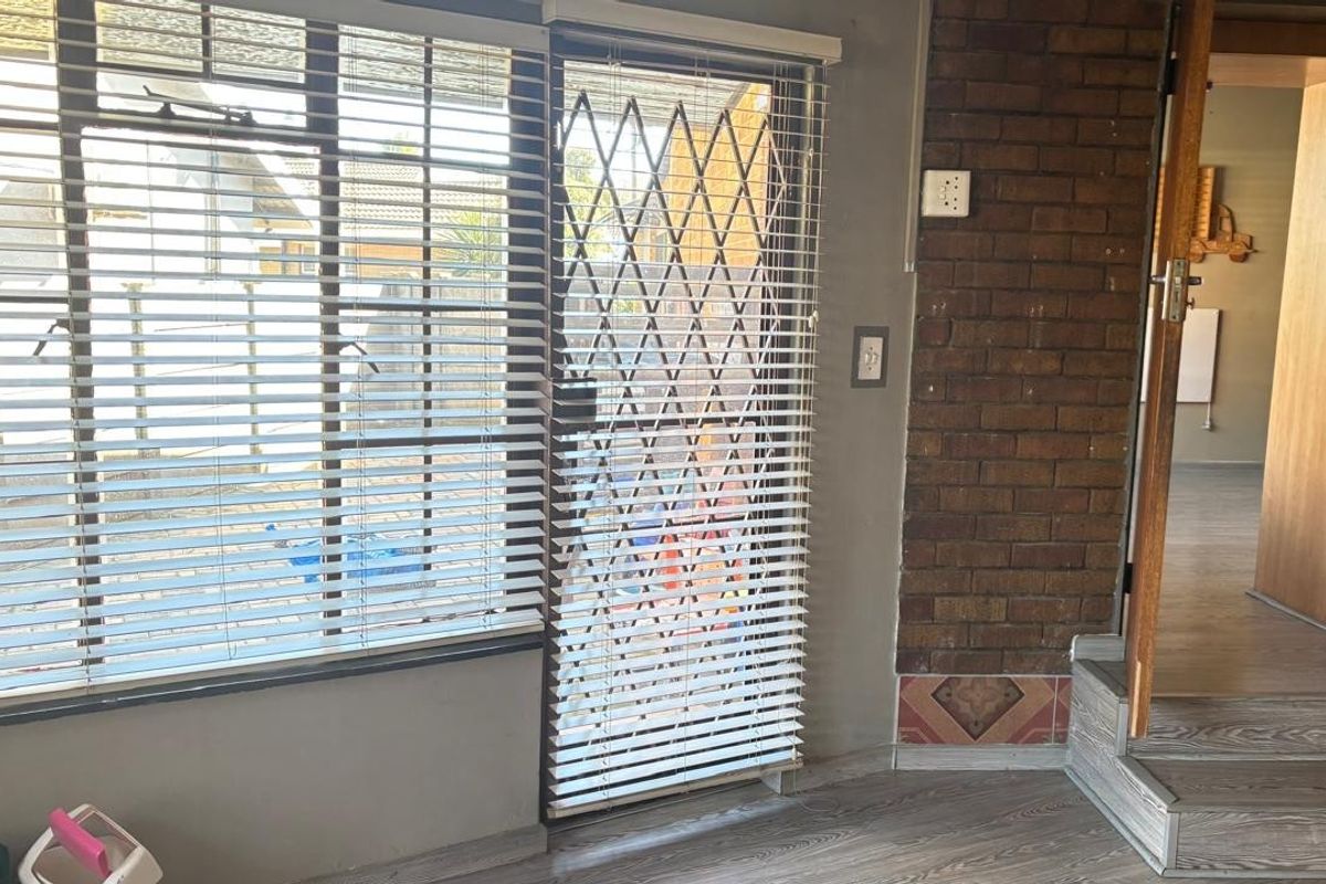 Living area featuring a brick accent wall, laminate flooring, and a security gate leading to the exterior.