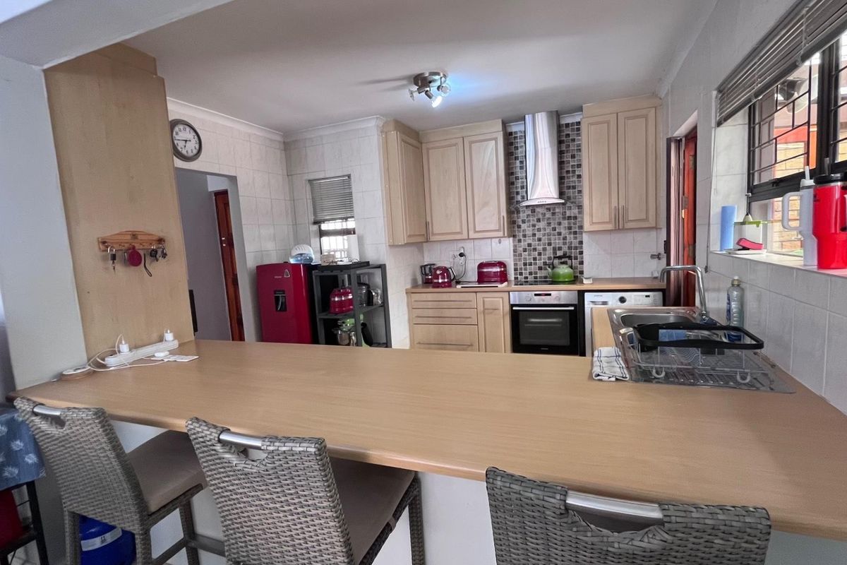 Functional kitchen featuring light wood cabinetry, a breakfast bar, stainless steel extractor fan, built-in oven, and tiled backsplash.