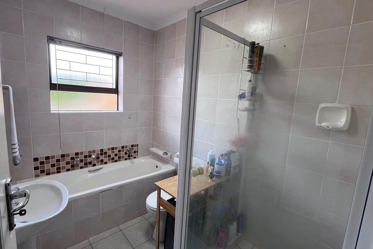 A functional bathroom featuring a built-in bathtub, separate glass-enclosed shower, pedestal basin, and toilet with neutral wall tiling.