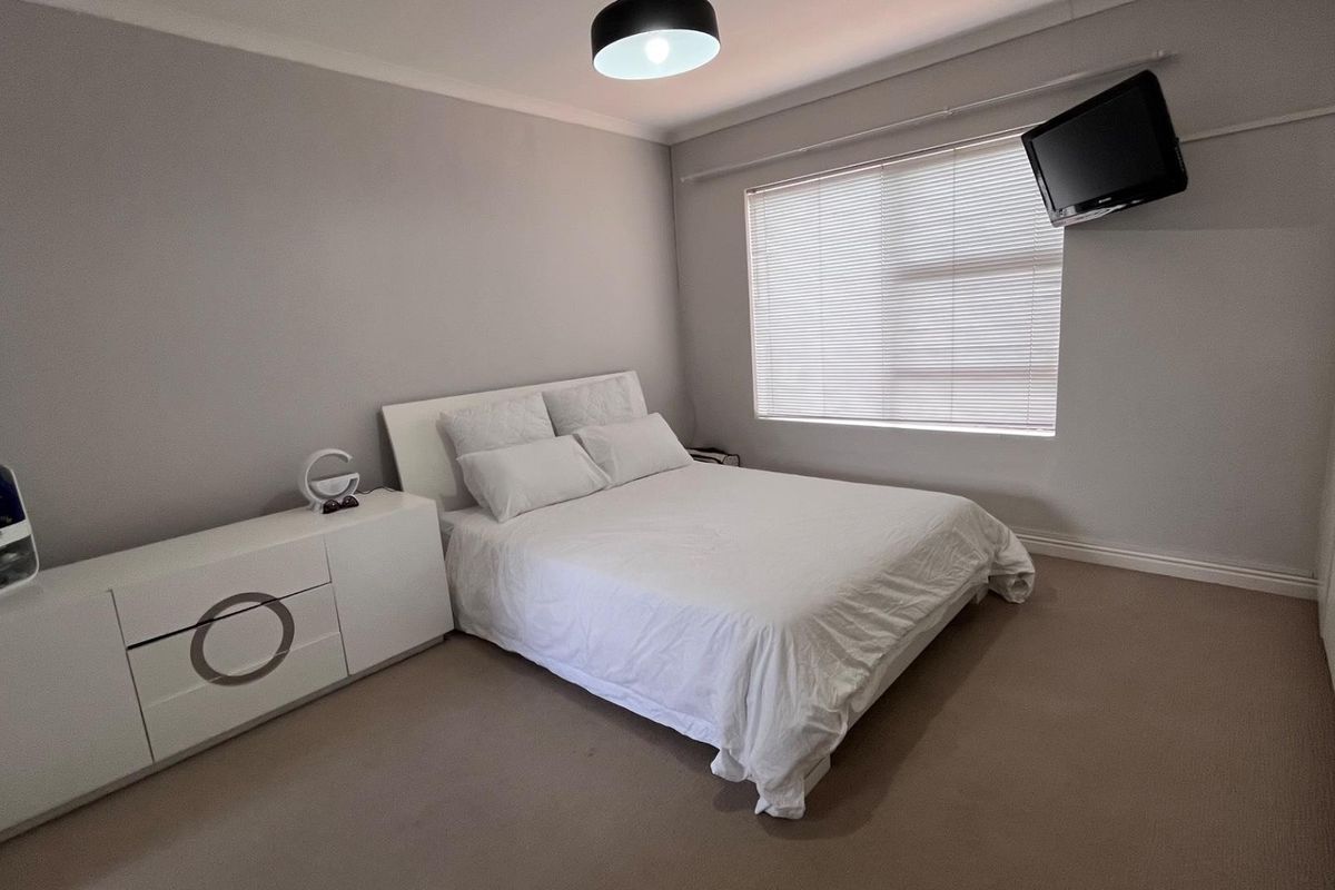 A neutrally decorated bedroom featuring fitted built-in cupboards, carpeted flooring, and a window with fitted blinds.