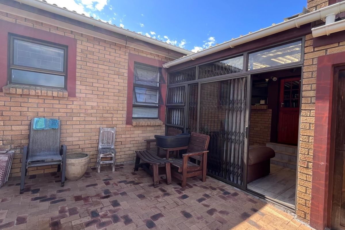 A paved rear patio area featuring brick wall construction, sliding glass doors with security gates, and access to the interior living space.