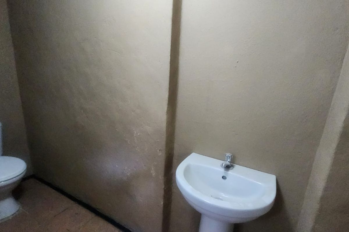 A basic bathroom featuring a standard pedestal basin and a toilet, with plain painted walls and tiled flooring.