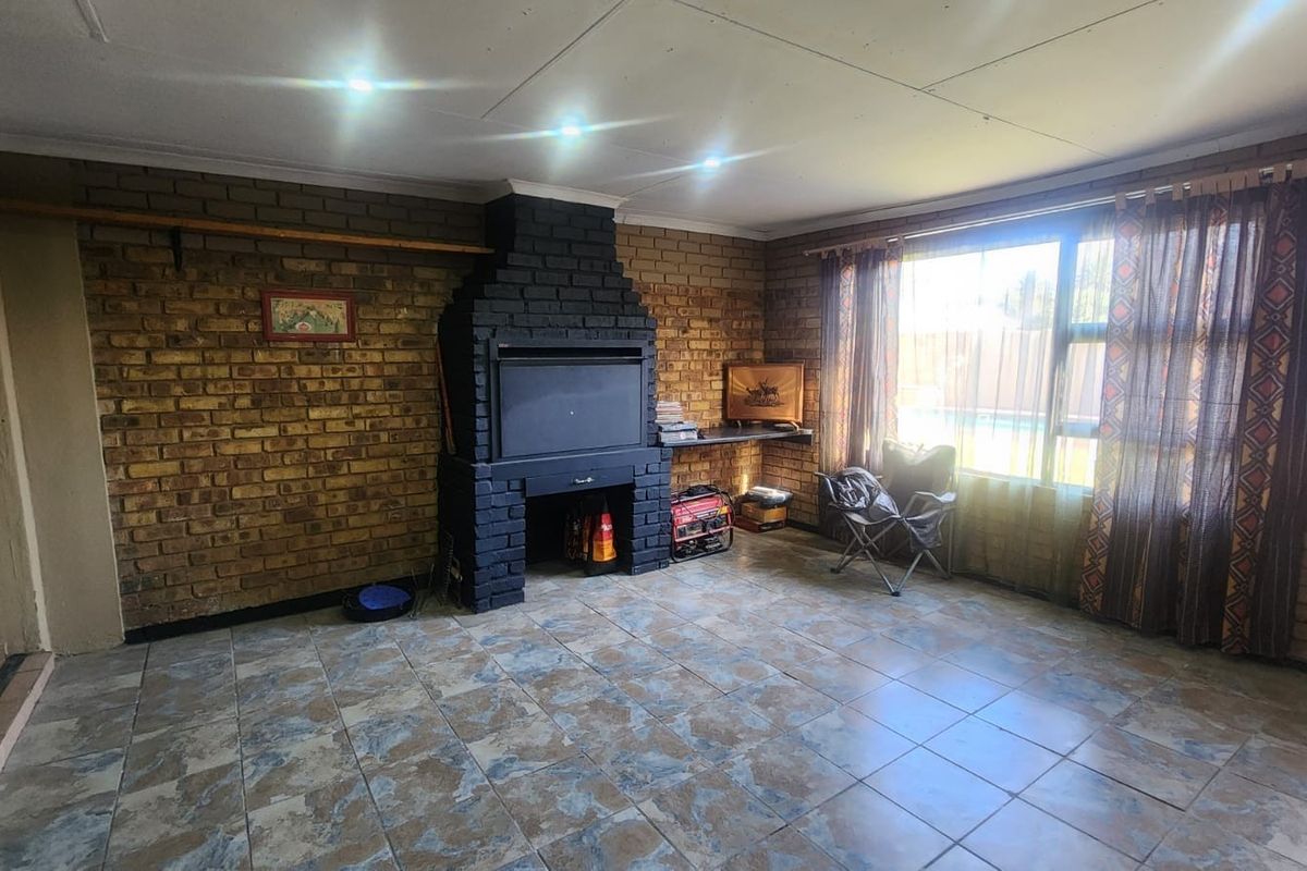 Spacious living area featuring exposed brick walls, a built-in fireplace, and tiled flooring with large windows providing natural light.