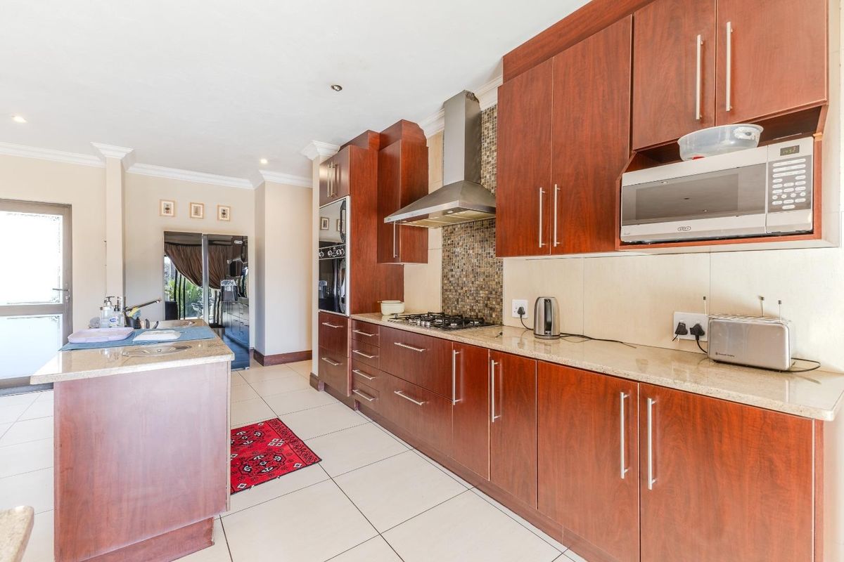 A functional kitchen featuring dark wood cabinetry, granite countertops, a built-in oven, gas hob, and a stainless steel extractor fan.