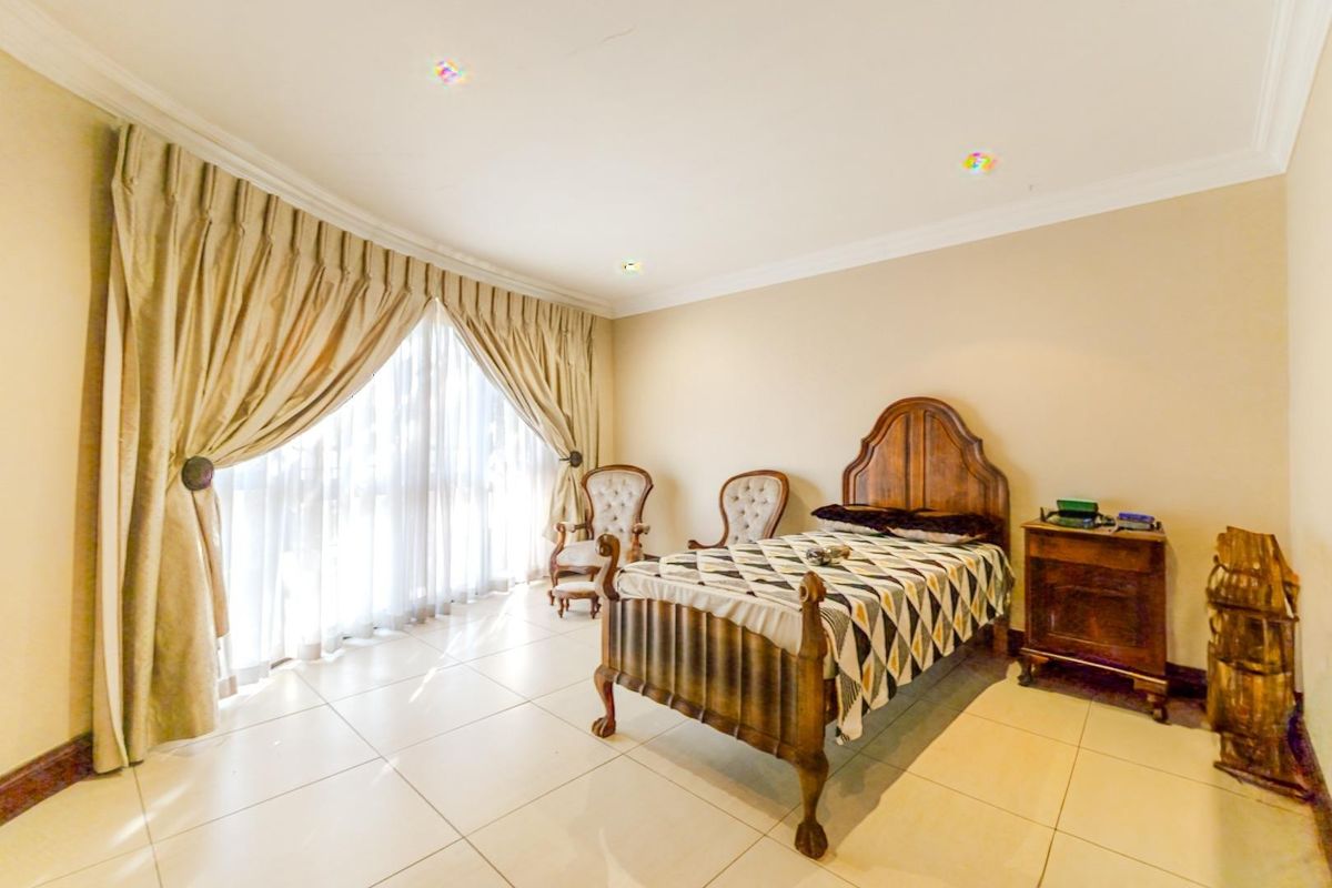 A spacious bedroom featuring large windows with floor-to-ceiling curtains and neutral tiled flooring.