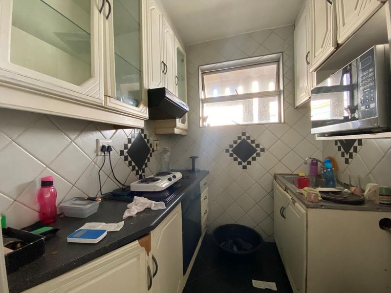 Compact kitchen featuring white cabinetry, dark countertops, built-in hob, and tiled backsplash, offering a functional layout in need of cosmetic updates.