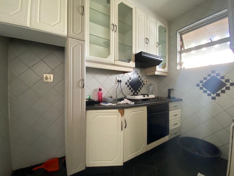 A compact kitchen featuring white cabinetry, built-in oven, gas hob, extractor fan, and diamond-patterned wall tiling.