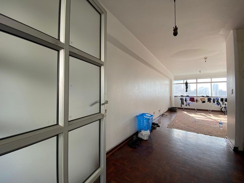 An open-plan living area featuring parquet flooring, large windows with city views, and a glass-paneled door entrance.