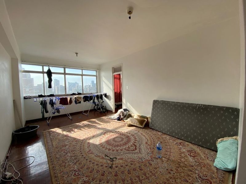A spacious living area featuring large windows with city views, wooden flooring, and ample natural light, offering a blank canvas for renovation.