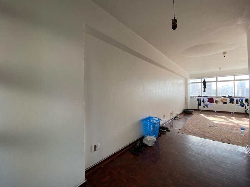 A spacious living area featuring dark parquet flooring, large windows providing natural light, and visible signs of ceiling water damage.