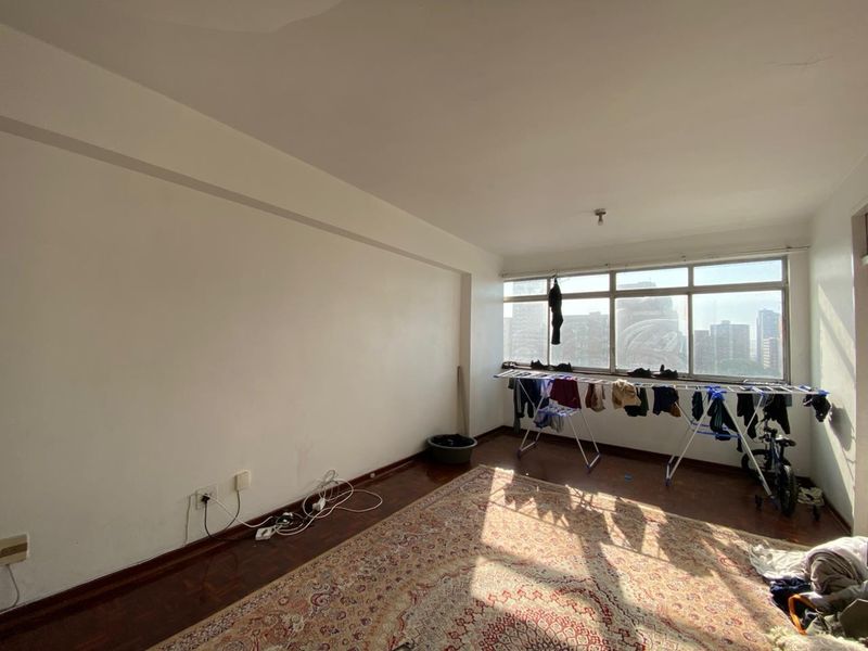 A bright, open living room featuring dark wood-style flooring, large windows with city views, and ample natural light.