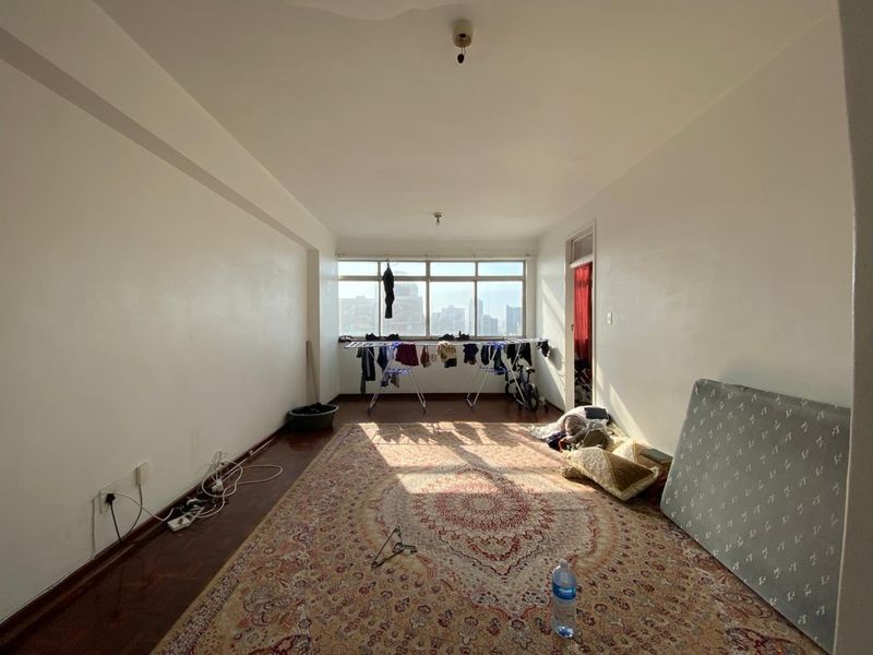 A spacious, empty living area featuring dark wood-style flooring and large windows that provide natural light and an urban view.