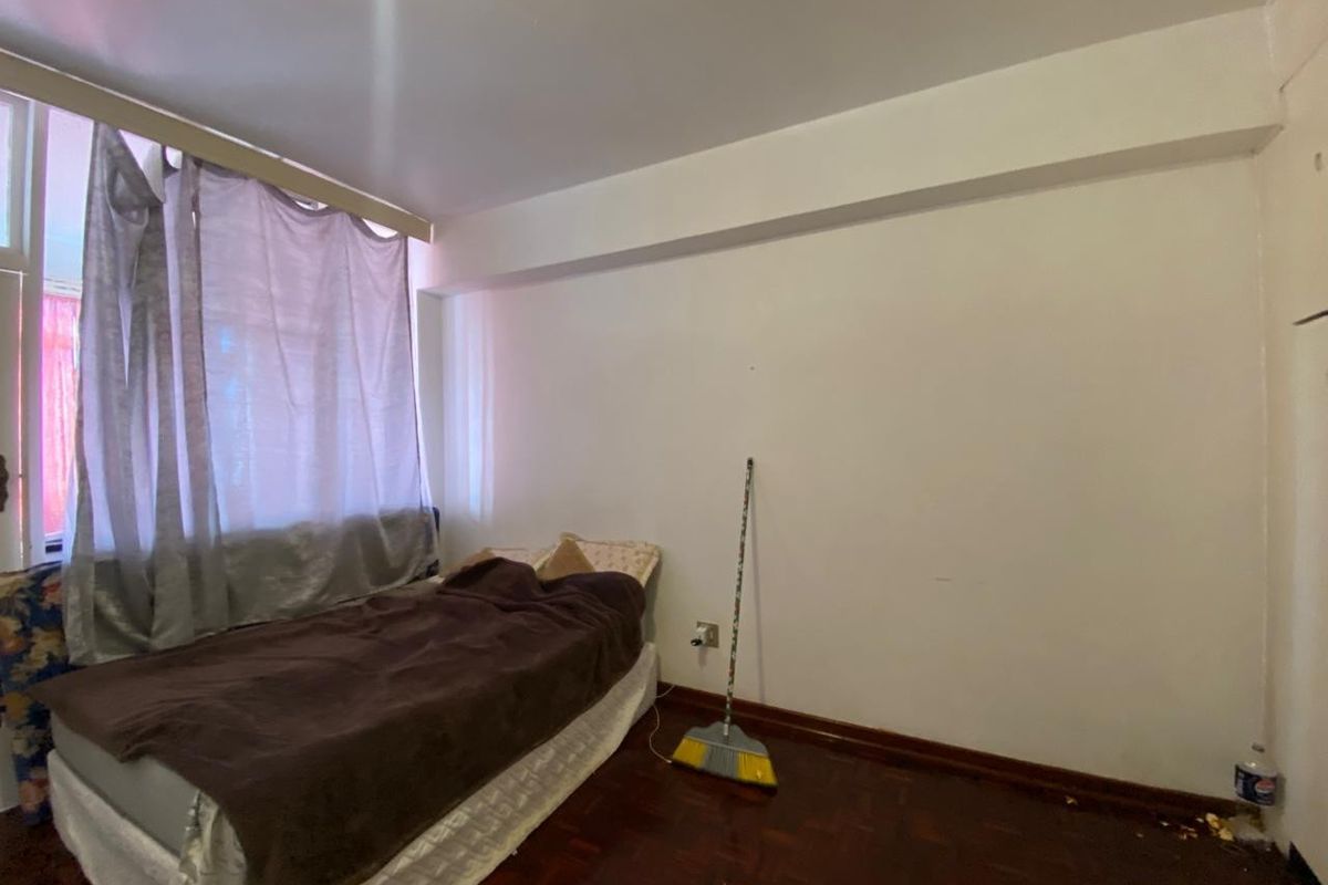 A bedroom featuring dark parquet flooring and a large window with curtains, providing natural light to the space.