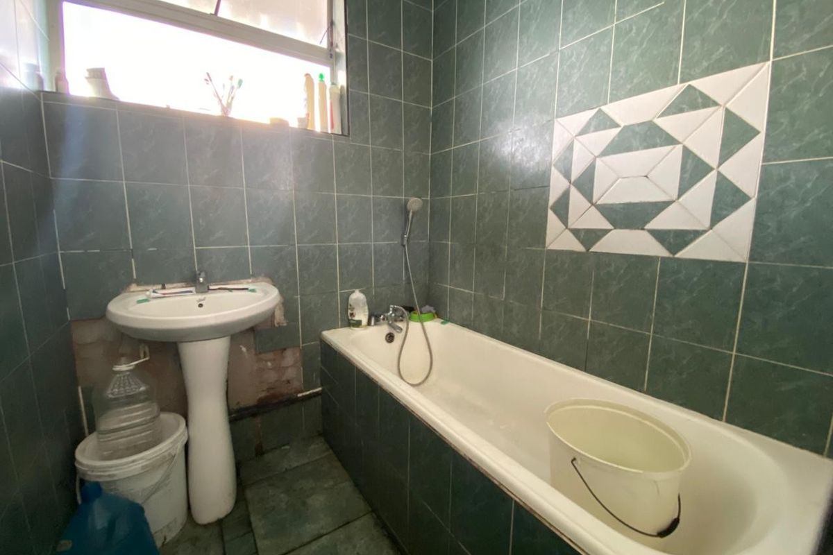 A dated bathroom featuring a bathtub with a handheld shower attachment and a pedestal basin, requiring renovation and tile repairs.