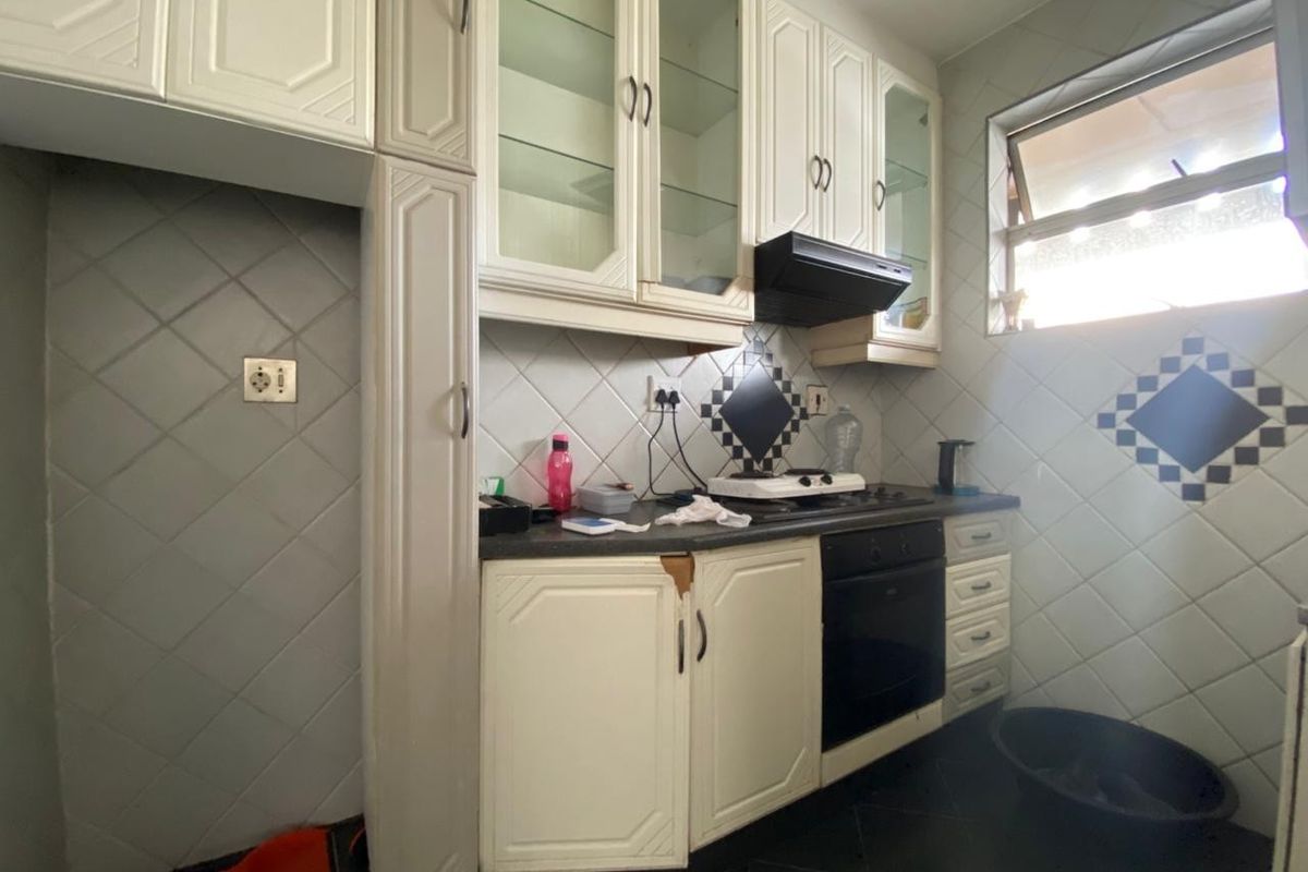 A compact kitchen featuring white cabinetry, built-in oven, gas hob, extractor fan, and diamond-patterned wall tiling.