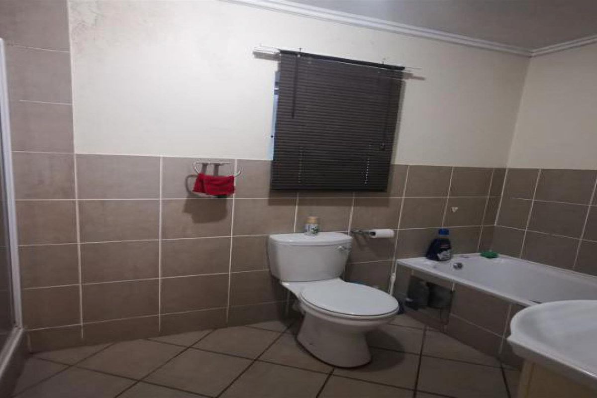 A functional bathroom featuring a shower enclosure, bathtub, and toilet, with tiled finishes. The space requires minor repairs to the bathtub panel and ceiling.