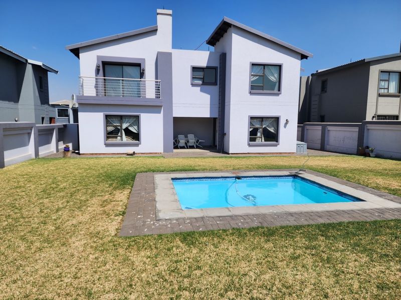 Rear view of a two-story residential house featuring a swimming pool, paved pool surround, and a covered patio area.