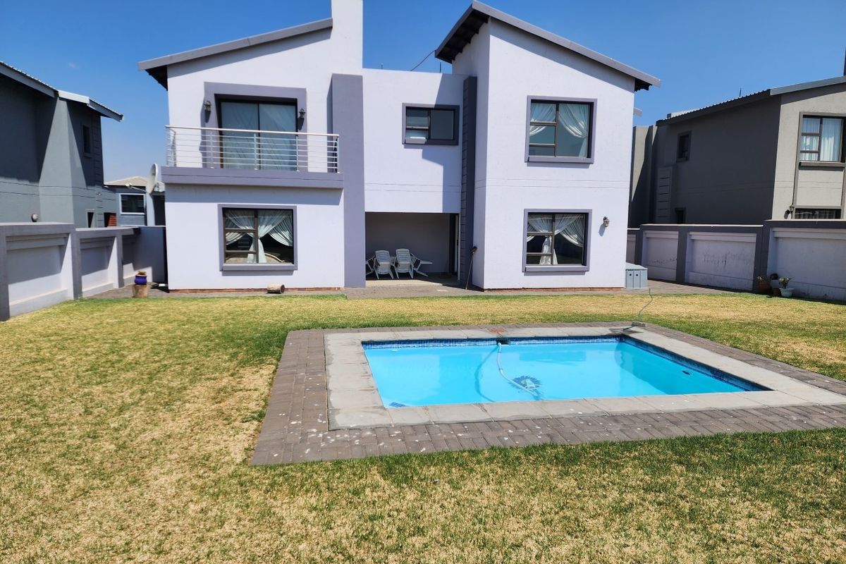 Rear view of a two-story residential house featuring a swimming pool, paved pool surround, and a covered patio area.