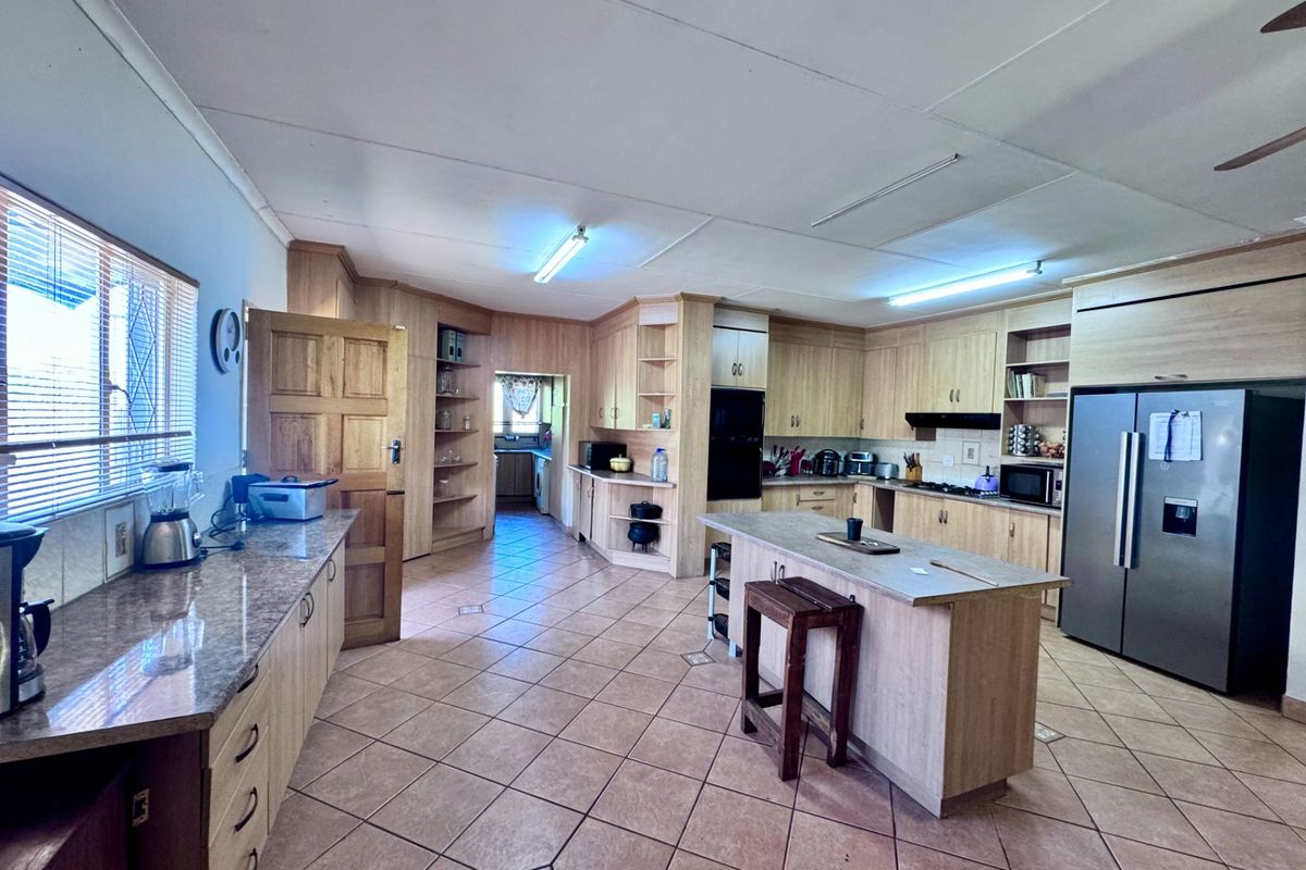 Spacious kitchen featuring light wood cabinetry, a central island, tiled flooring, and an adjoining scullery area.