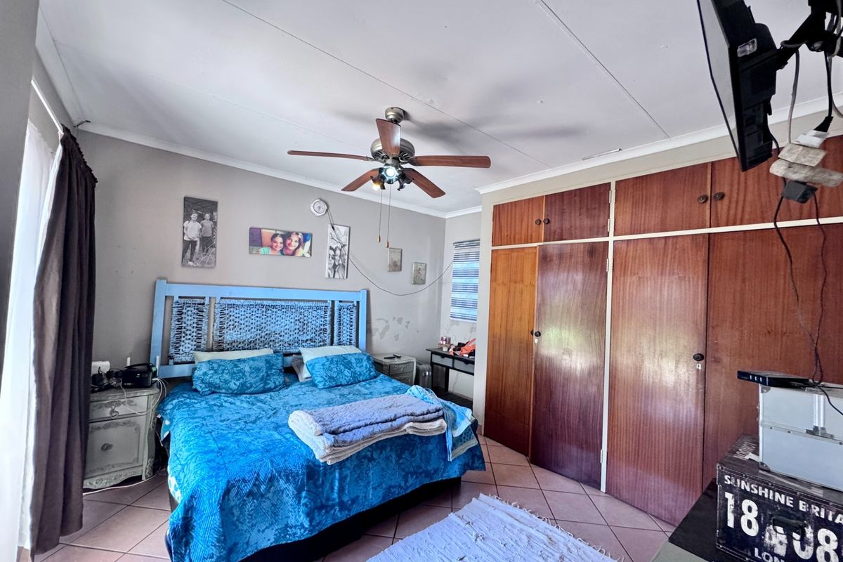 A bedroom featuring built-in wooden cupboards, a ceiling fan, and tiled flooring.