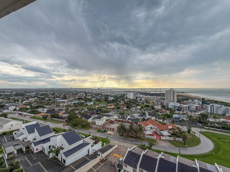 Elevated panoramic view overlooking the surrounding residential neighborhood, coastal landscape, and distant harbor under a dramatic cloudy sky.