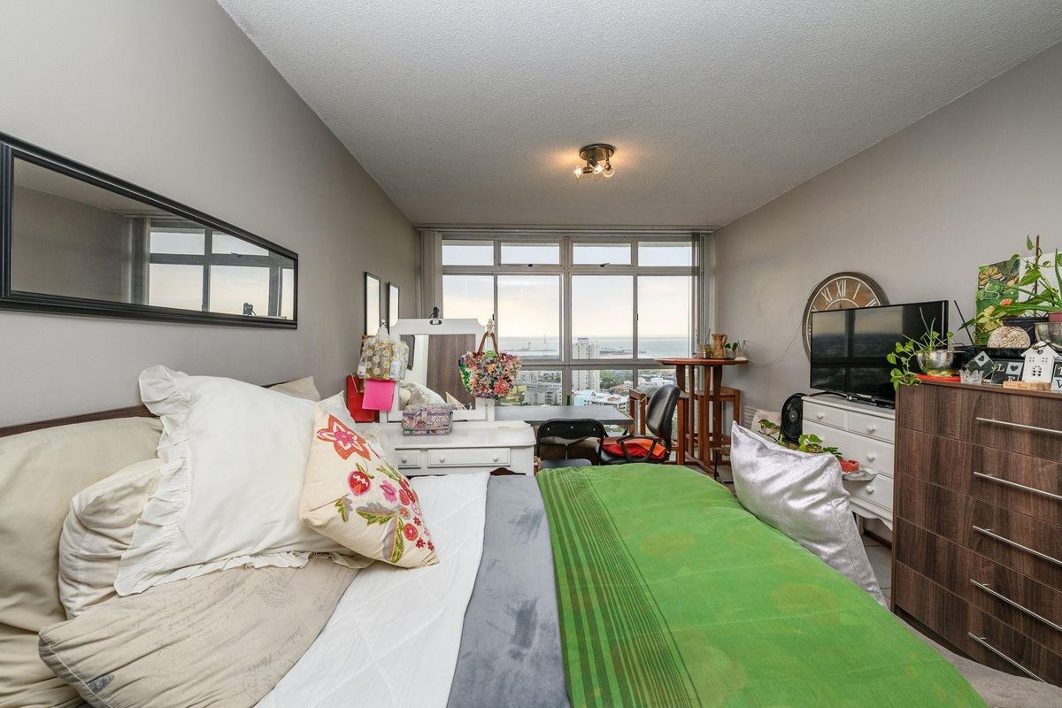 A bedroom featuring large windows with expansive city and coastal views, providing ample natural light and a spacious feel.