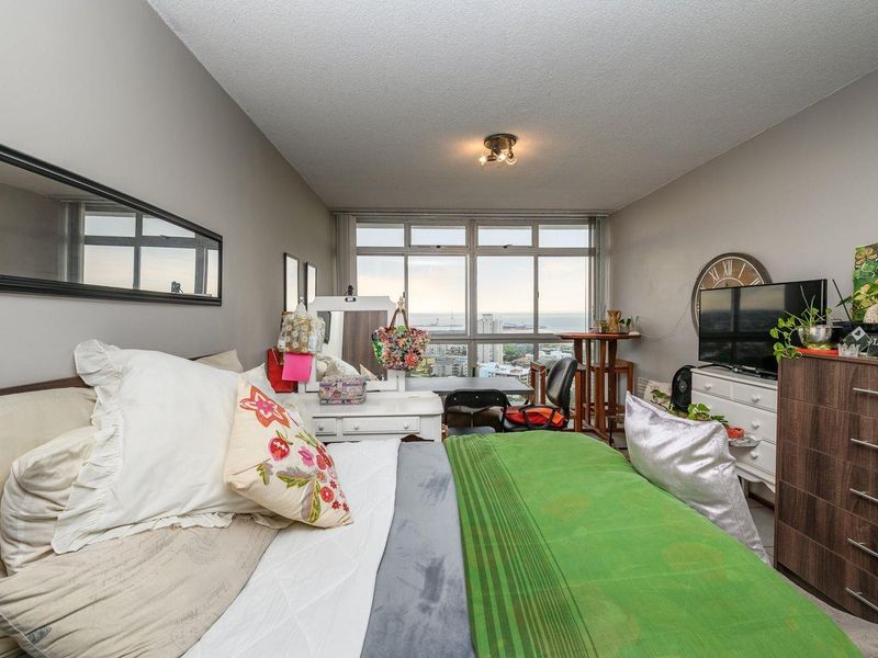 A bedroom featuring large windows with expansive city and coastal views, providing ample natural light and a spacious feel.