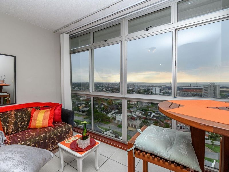 An enclosed balcony featuring tiled flooring and large aluminum-framed windows offering expansive city and coastal views.