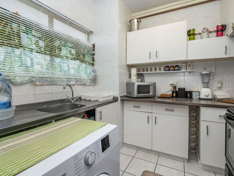 A functional kitchen featuring white cabinetry, tiled backsplash, laminate countertops, and a stainless steel sink with integrated laundry appliance space.