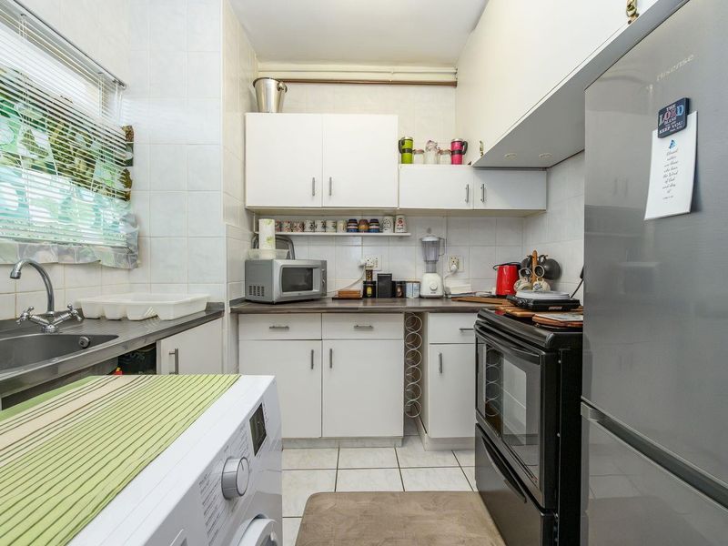 Compact kitchen featuring white cabinetry, laminate countertops, tiled backsplash, and integrated laundry plumbing, offering a functional and efficient workspace.