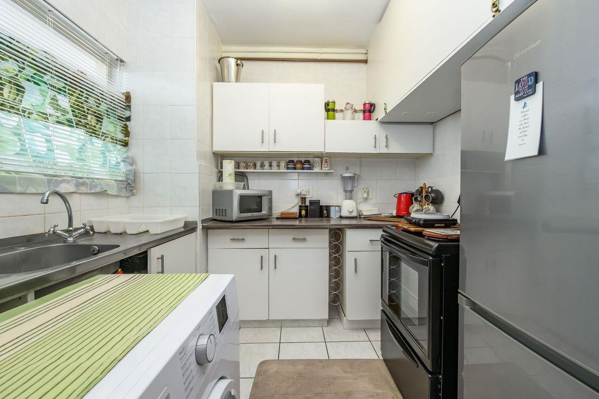 Compact kitchen featuring white cabinetry, laminate countertops, tiled backsplash, and integrated laundry plumbing, offering a functional and efficient workspace.