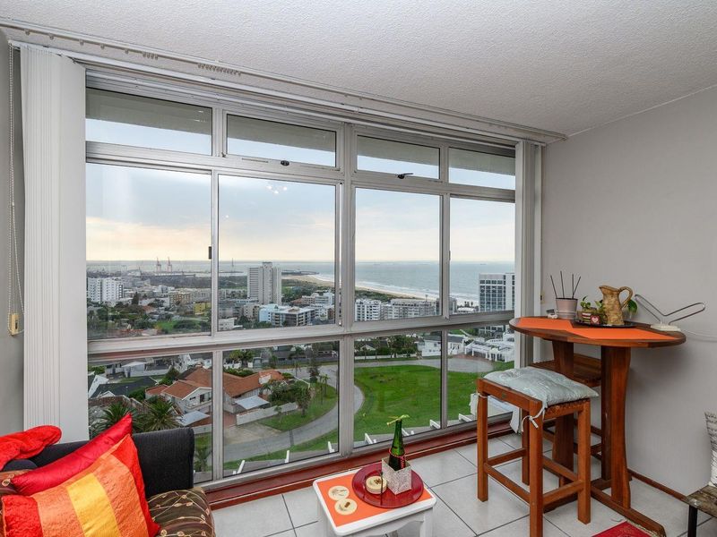 Living area featuring expansive floor-to-ceiling windows with panoramic coastal and city views, tiled flooring, and a neutral interior palette.