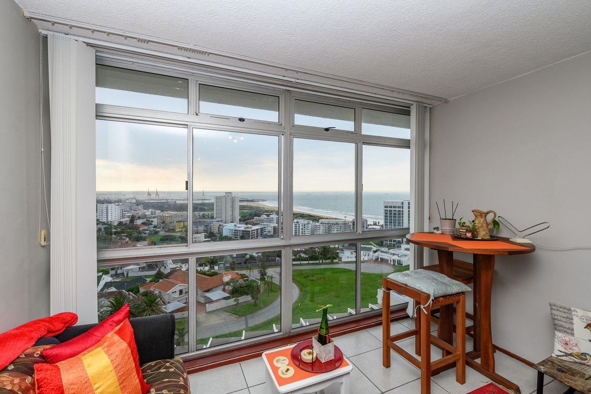 Living area featuring expansive floor-to-ceiling windows with panoramic coastal and city views, tiled flooring, and a neutral interior palette.