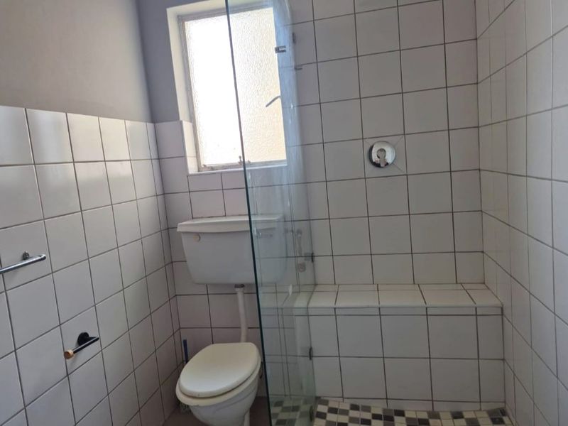 A functional bathroom featuring a tiled shower enclosure with a glass screen, a standard toilet, and tiled wall finishes.