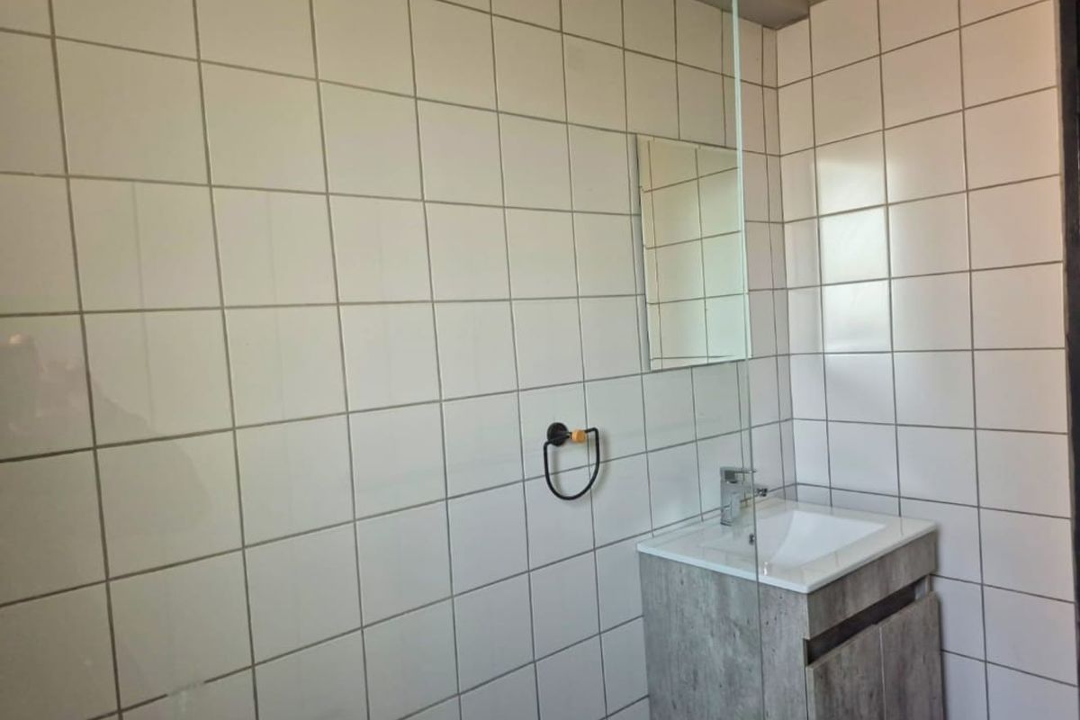 A modern bathroom featuring white wall tiles, a vanity cabinet with a basin, and a glass shower screen.