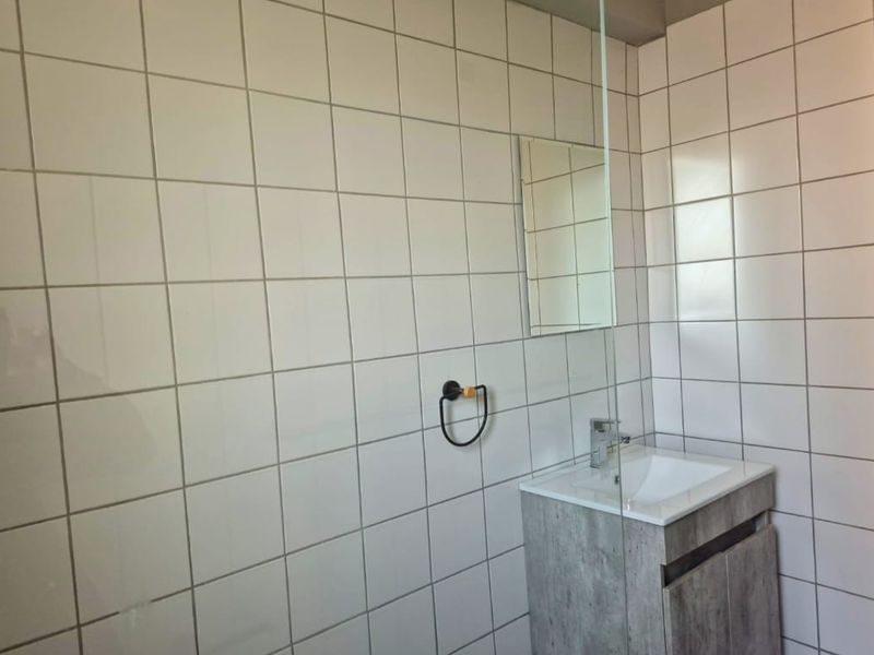 A modern bathroom featuring white wall tiles, a vanity cabinet with a basin, and a glass shower screen.