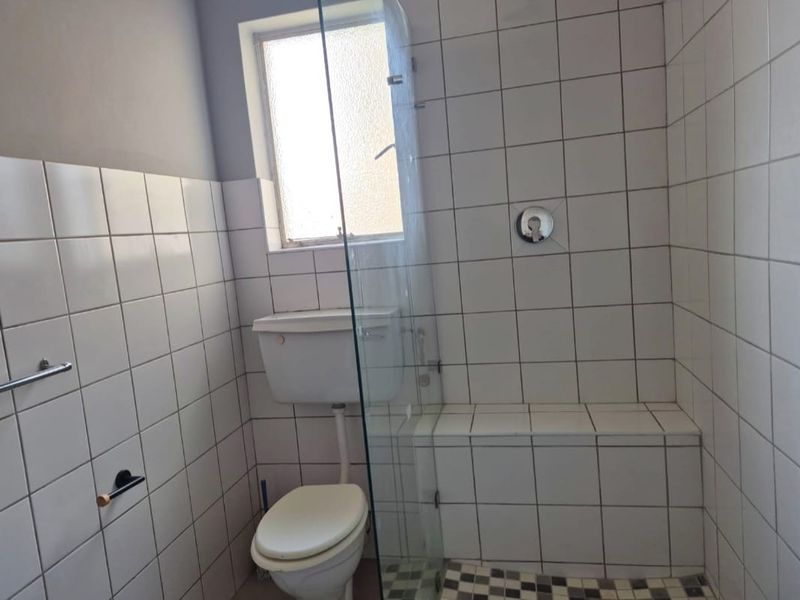 A functional bathroom featuring a tiled shower enclosure with a built-in bench, glass screen, and a standard toilet.
