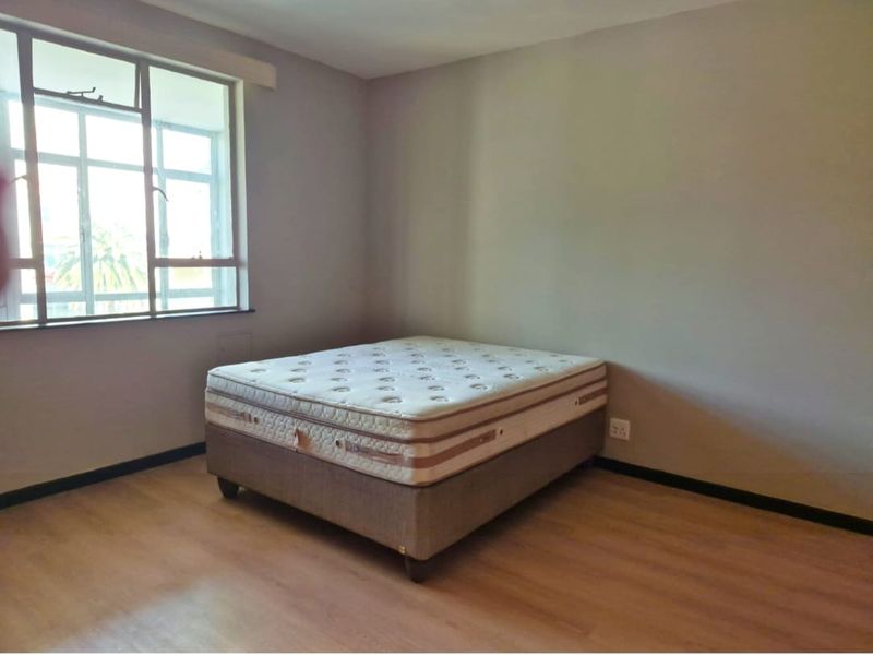 A simple bedroom featuring laminate flooring, neutral wall tones, and a large window providing natural light.