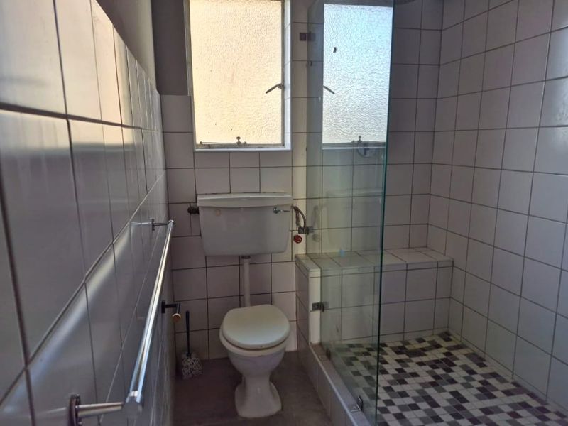 A functional bathroom featuring a shower enclosure, toilet, and tiled finishes throughout, offering a blank canvas for potential modernization and renovation.