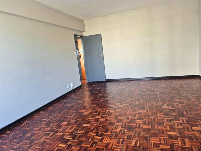 An empty living room featuring traditional parquet flooring and neutral wall finishes, providing a blank canvas for interior design.